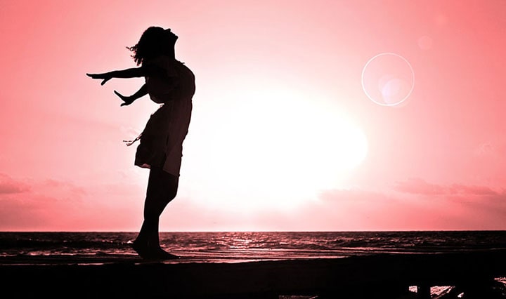Imagen de una joven en un atardecer en la playa haciendo un movimiento de liberación tras recibir Terapia Individual